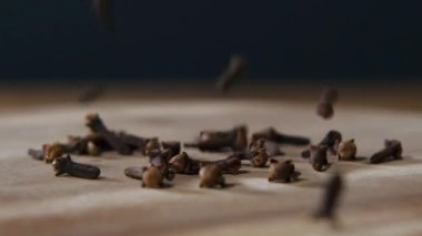 Kuru karanfiller yavaş çekimde siyah arkaplan üzerine koyu kırsal ahşap masaya düşüyor. Baharatlı yemek malzemesi..