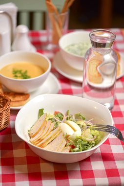 Beyaz kasede servis edilen Sezar usulü tavuk salatası. Tavuk etli, yumurtalı, domatesli geleneksel salata. Restoranda akşam yemeği.