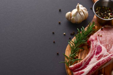 Taze çiğ biftek ahşap kesim tahtasında siyah arka planda baharatlarla, üst manzara.