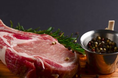 Taze çiğ biftek ahşap kesim tahtasında siyah arka planda baharatlarla, üst manzara.