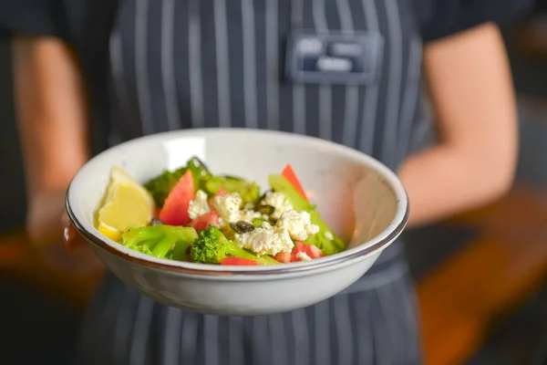 Close up de garçom servindo um prato de salada de legumes com queijo feta, alface e tomate. Serviço de restaurante . — Fotografia de Stock
