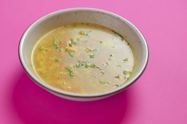 Parlak pembe arka planda izole edilmiş bir kasede servis edilen yumurtalı sebze çorbası..