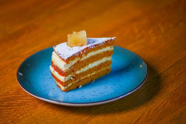 Katmanlı vanilyalı ballı kek, bulanık restoranın arka planında, ahşap bir masada mavi bir tabakta servis ediliyor..