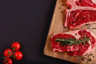 Taze çiğ biftek ahşap kesim tahtasında siyah arka planda baharatlarla, üst manzara.