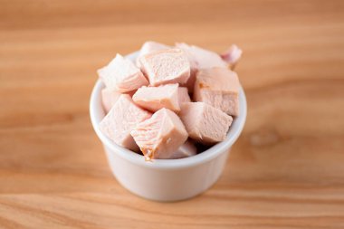 Tahta arka planda küçük beyaz bir kasede kesilmiş jambon kasesi. Atıştırmalık, aperatif. Uzay afişini kopyala. Pizza malzemesi.