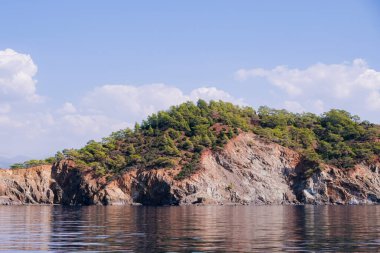 Huzurlu deniz manzarası. Sakin denizin üzerindeki güzel mavi gökyüzü ve güneş ışığı yansıması. Deniz dalgaları. Ufuktaki dağlar.