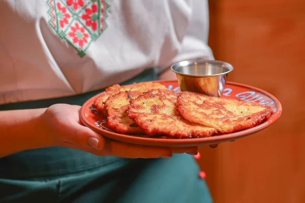 Potato pancakes dranik with sour cream, traditional Ukrainian dish. Waiter in traditional uniform serving dranyki. — Stock Photo, Image