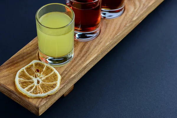 Chilled vodka cocktail drinks with spices on rustic wooden board over black background. Flat lay, top view, copy space.