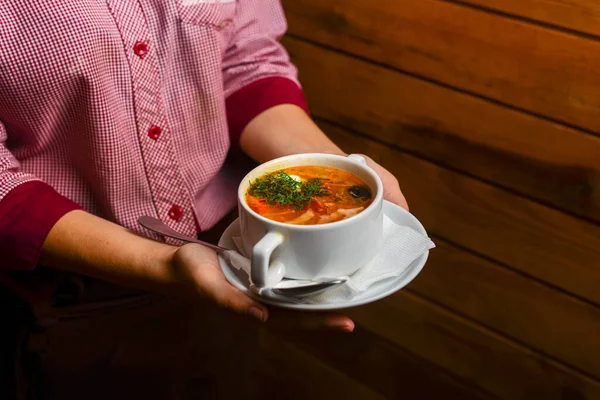 Мужчина держит миску супа. Официант подает свежий горячий суп в закусочной или ресторане. Здоровый вкусный ужин . — стоковое фото