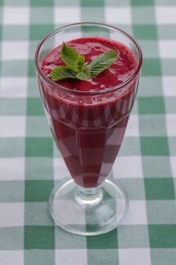 Yeşil ekose masa örtüsünde servis edilen tropik bir içecek, böğürtlen ve nane kokteyli..