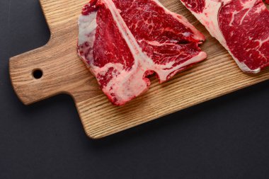 Fresh raw beef steak on wooden cutting board, top view. Served over black background.