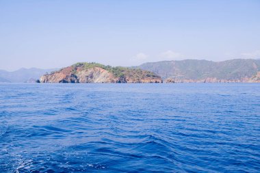 Huzurlu deniz manzarası. Sakin denizin üzerindeki güzel mavi gökyüzü ve güneş ışığı yansıması. Deniz dalgaları. Ufuktaki dağlar.