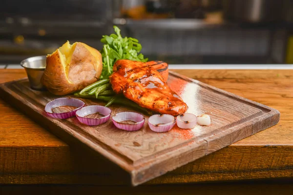 Medium zeldzame gegrilde biefstuk met geroosterde aardappelpartjes en groene salade op snijplank op houten ondergrond. — Stockfoto