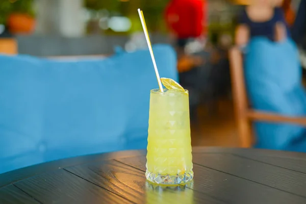 Cóctel de alcohol frío de verano con hielo y naranja en un vaso alto sobre una mesa de madera sobre fondo borroso del restaurante . — Foto de Stock