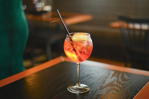 Koude zomer alcohol cocktail met ijs en sinaasappel in een hoog glas op houten tafel op wazig restaurant achtergrond. — Stockfoto