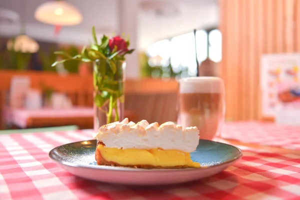 Piece of cream lemon meringue pie served with Latte coffee on a table with red plaid tablecloth. — Stock Photo, Image
