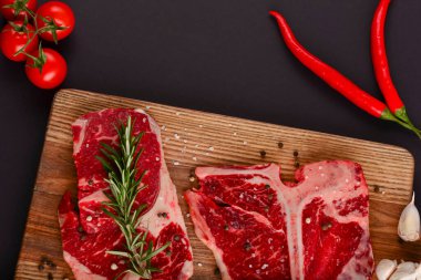 Taze çiğ biftek ahşap kesim tahtasında siyah arka planda baharatlarla, üst manzara.