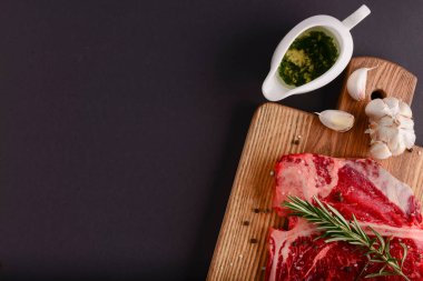 Taze çiğ biftek ahşap kesim tahtasında siyah arka planda baharatlarla, üst manzara.