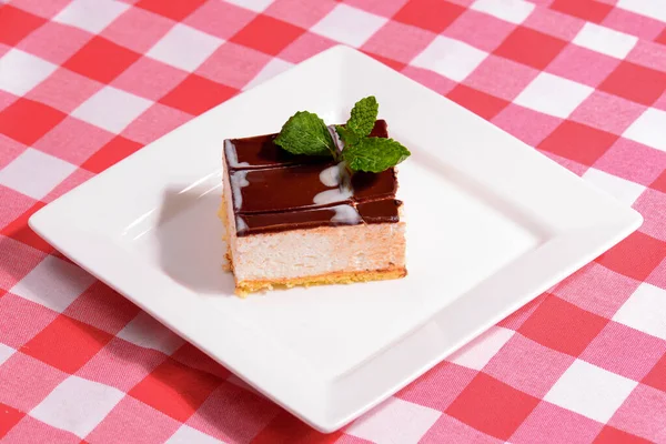 Rebanada de pastel de queso de Nueva York con chocolate y menta en un plato blanco sobre fondo a cuadros en un restaurante. Postre dulce —  Fotos de Stock
