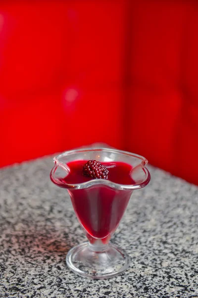 Cseresznye lekvár málnával tálalva magas pohárban egy márványasztalon homályos háttérrel. — Stock Fotó