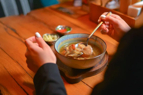 Молодая женщина ест суп, подаваемый в белой миске. Ужинаю. Концепция ресторана. Женская рука держит ложку . — стоковое фото