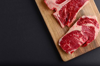Fresh raw beef steak on wooden cutting board, top view. Served over black background.