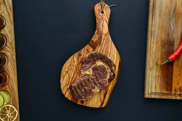 Bife de carne fresca e temperos em tábua de madeira rústica sobre fundo preto. Vista superior, flat lay, copiar banner espaço . — Fotografia de Stock