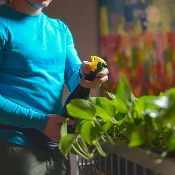 Mann in blauer Uniform gießt Blumen in Restaurant. Kellner bei der Arbeit. — Stockfoto