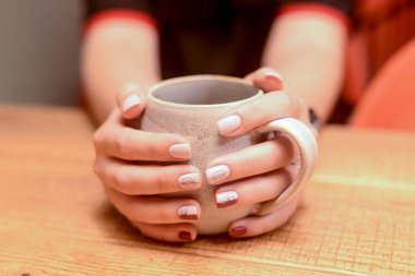 Kahve ya da çay içen genç bir kadın, ellerini fincanda ısıtıyor. Durgun bir hayat, dışarıda yemek..