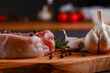 Taze çiğ biftek ahşap kesim tahtasında siyah arka planda baharatlarla, üst manzara.