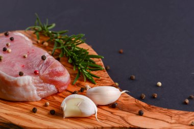 Taze çiğ biftek ahşap kesim tahtasında siyah arka planda baharatlarla, üst manzara.