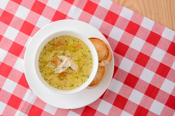 Sopa de frango com legumes e carne servida em uma tigela branca sobre fundo de madeira rústica com toalha de mesa xadrez vermelho . — Fotografia de Stock