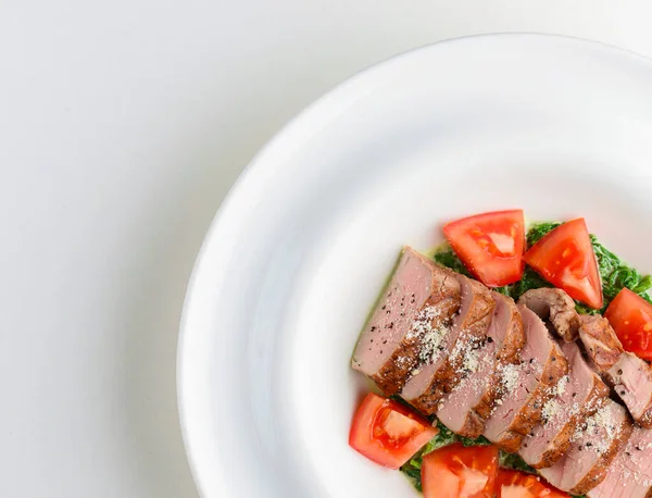 Carne de cerdo asada al horno cortada en rodajas, servida en un plato blanco con tomates frescos y verdura cruda . — Foto de Stock