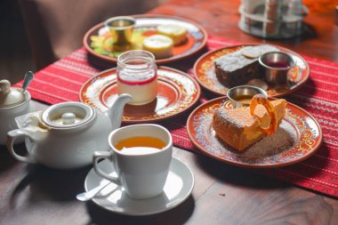 Tatlı tatlılı çay saati için masa hazır. Çikolatalı kek, vanilyalı kek, panna cotta. Çay demliği ve tatlı çay..