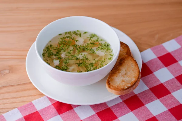 Sup ayam dengan sayuran dan daging disajikan dalam mangkuk putih di atas kayu berkarat dengan taplak meja merah. — Stok Foto