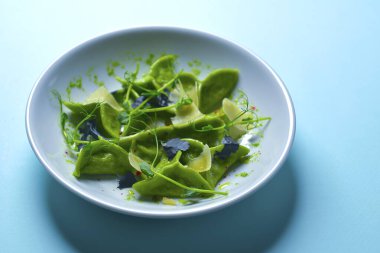 Yeşil ıspanaklı İtalyan mantısı, ricotta peyniri ve et dolgulu. Pastel mavi arka planda mavi bir tabakta servis ediliyor..