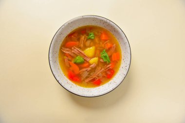 Beyaz bir kasede servis edilen et ve sebzeli lezzetli yahni çorbası parlak pastel sarısı arka planda. Sağlıklı beslenme.