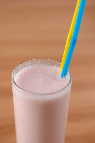 Vanilla strawberry milkshake in a tall galss with two plastic straws on light rustic wooden table. — Stock Photo, Image
