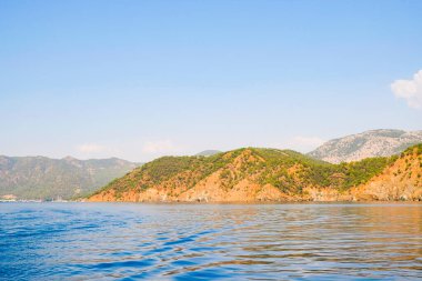 Huzurlu deniz manzarası. Sakin denizin üzerindeki güzel mavi gökyüzü ve güneş ışığı yansıması. Deniz dalgaları. Ufuktaki dağlar.
