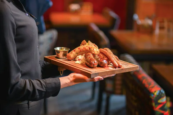 Sluiten van serveerster in zwart uniform serveert worst en aardappel aan een gast tijdens de lunch in een pub. — Stockfoto