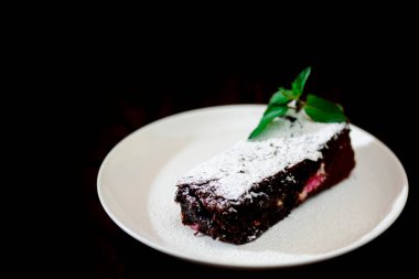 Nane yapraklarıyla süslenmiş beyaz tabakta çikolatalı kek ve siyah arka planda şeker tozu.