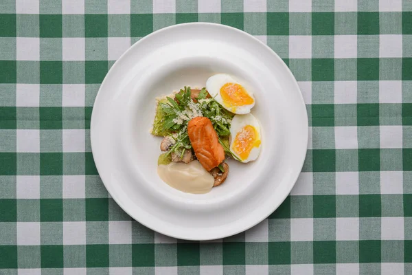 Grillad röd fiskbiff och kokta ägg serveras i en vit tallrik över grön rutig duk. Italiensk mat, koncept. — Stockfoto