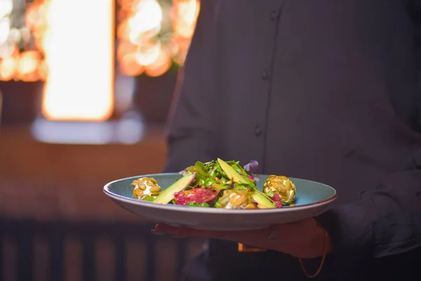 Garçom em uniforme preto, camisa, trazendo o espinafre saudável ordenado e salada de arugula com abacates . — Fotografia de Stock