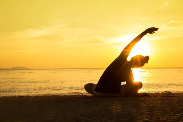 Silueta joven practicando yoga en la playa al atardecer . — Foto de Stock