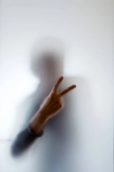 Bulanık yapma barış işareti buzlu cam arkasında bir adam figürü — Stok fotoğraf