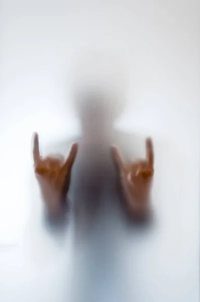 Homem fazendo um gesto de rocha atrás de um vidro fosco — Fotografia de Stock