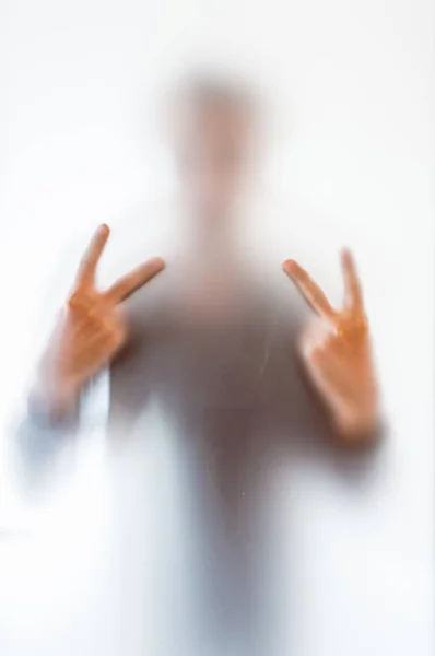 Fuzzy postava muže dělat znamení míru za matným sklem — Stock fotografie