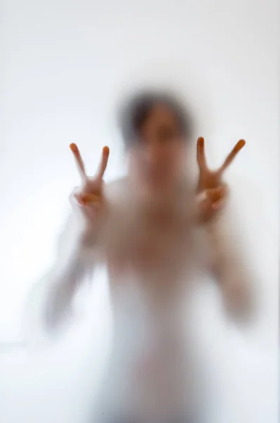 Verschwommene Figur einer Frau, die hinter Milchglas Friedenszeichen macht — Stockfoto