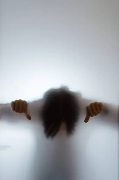 Blurry figure of a woman with thumbs down behind frosted glass — Stock Photo, Image