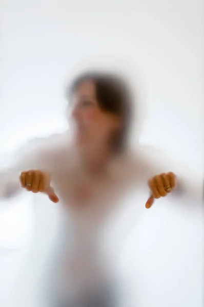 Figura embaçada de uma mulher com polegares para baixo atrás de vidro fosco — Fotografia de Stock